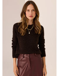 Woman wearing a dark sweater and maroon pants against a plain background