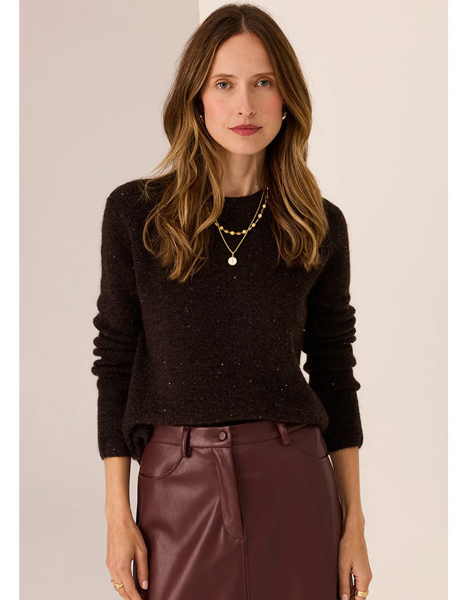 Woman wearing a dark sweater and maroon pants against a plain background