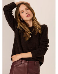 Woman wearing a dark sweater and maroon pants against a plain background