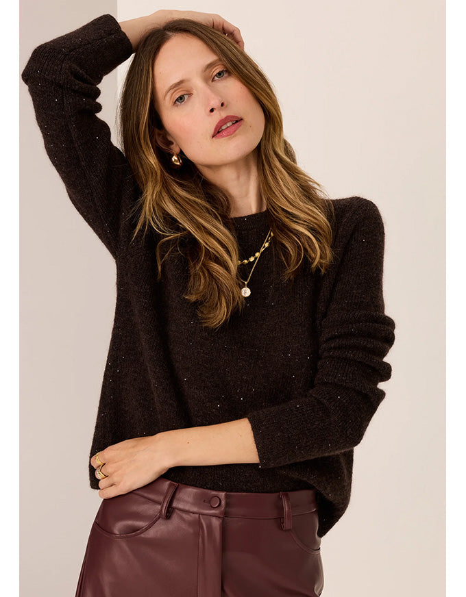 Woman wearing a dark sweater and maroon pants against a plain background