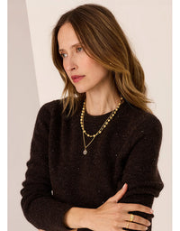 Woman wearing a black sweater and gold jewelry against a plain background