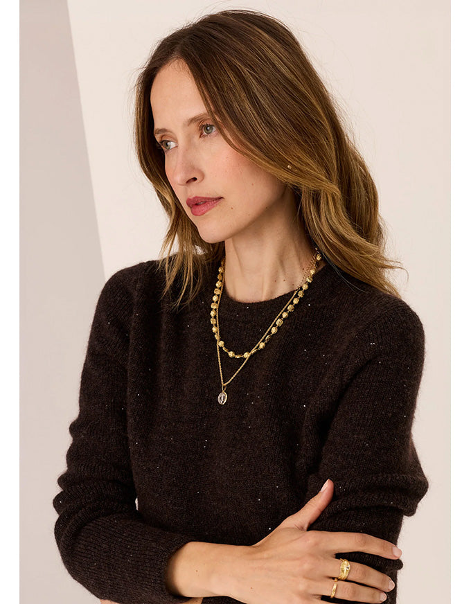 Woman wearing a black sweater and gold jewelry against a plain background
