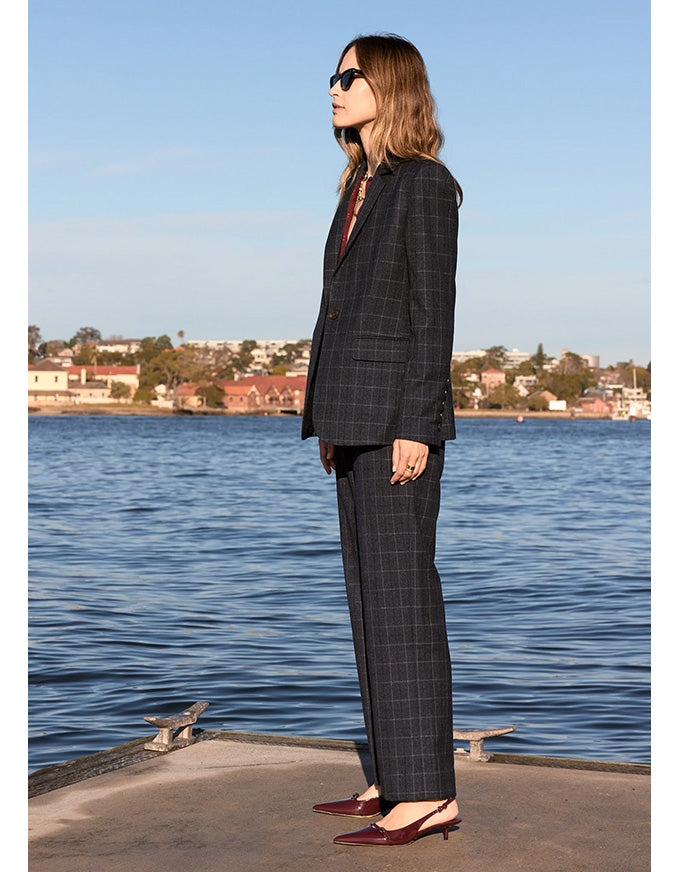 Woman in a checkered suit standing by a waterfront with a clear blue sky.
