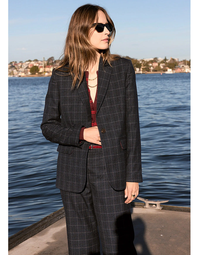 Woman in a checkered suit standing by a waterfront with sunglasses on