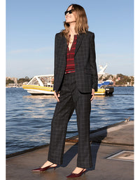 Woman in a checkered suit standing by a waterfront with boats in the background