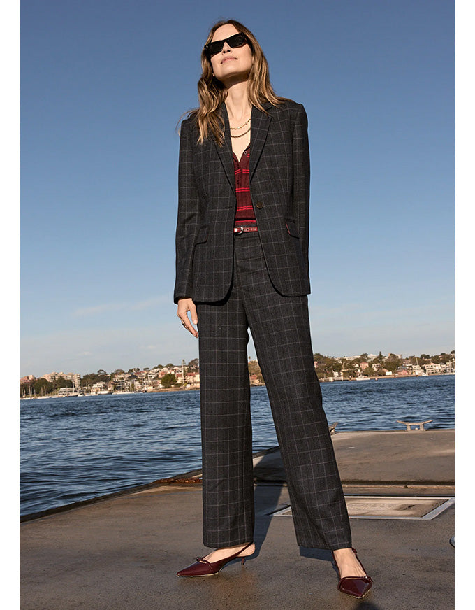 Woman in a checkered suit standing by a waterfront with clear blue sky.