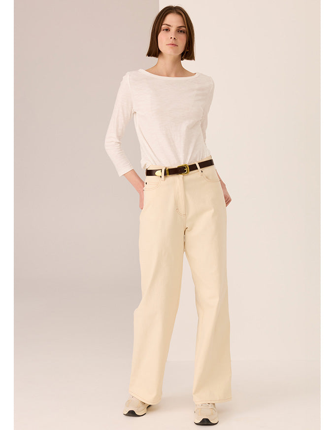 Woman wearing a white top and beige pants with a belt on a plain background