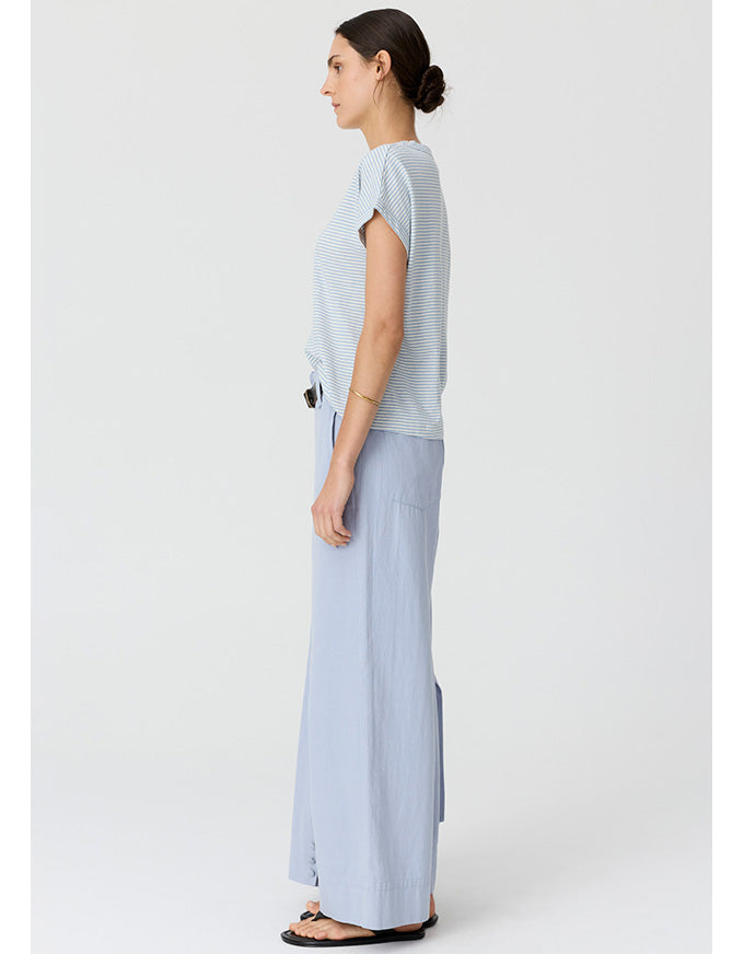 A woman shown in profile wearing a light blue and white striped short-sleeve top with matching wide-leg light blue pants, standing against a plain light gray studio background.