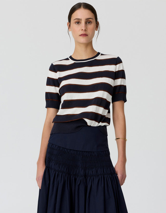 A model wearing a short-sleeve knit top with horizontal navy and off-white stripes, paired with a dark navy skirt, against a light gray studio background.