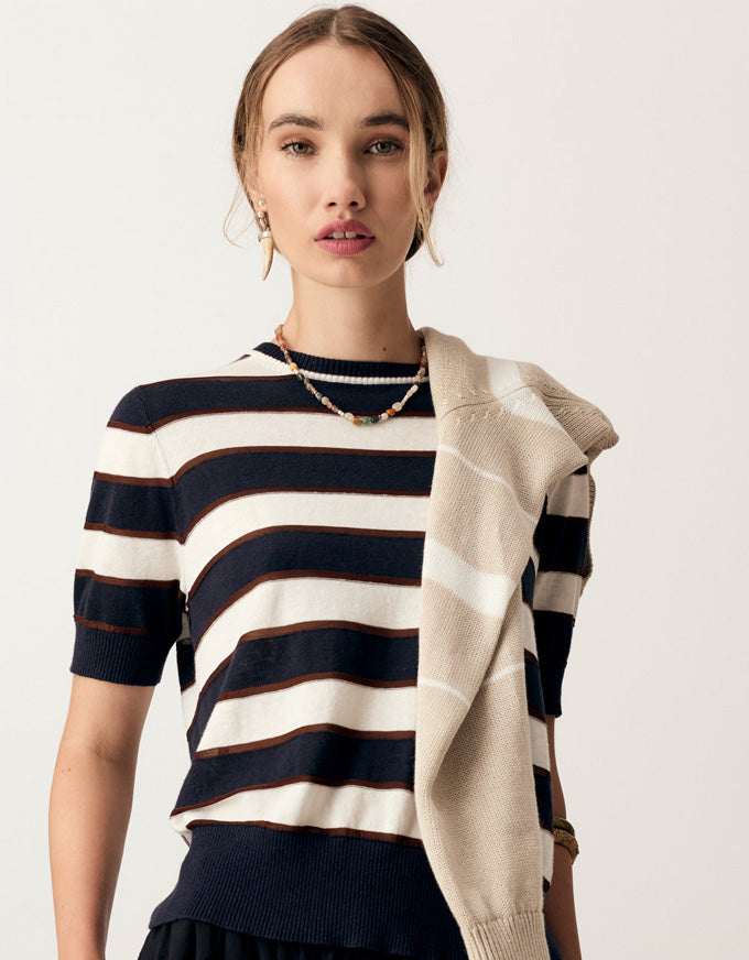 A woman wearing a navy and cream striped short-sleeve knit top with a beige knit shawl draped over one shoulder, photographed against a plain light background.