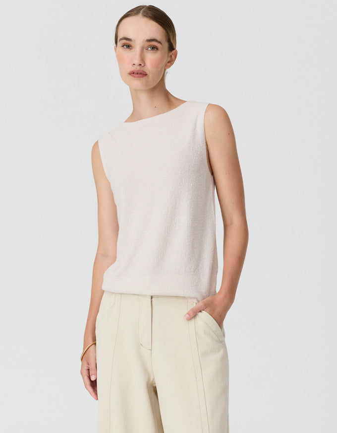 A woman modeling a sleeveless knit top in a light cream color, paired with matching cream trousers, against a solid light gray background.