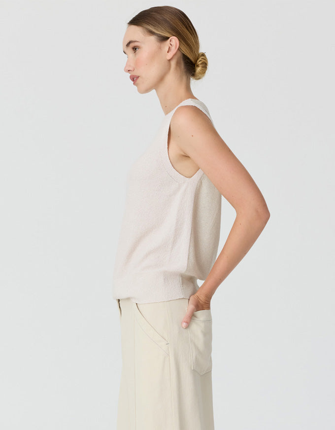 A woman shown in side profile wearing a sleeveless knit top and matching wide-leg pants in a light cream or off-white color, against a plain light gray studio background.