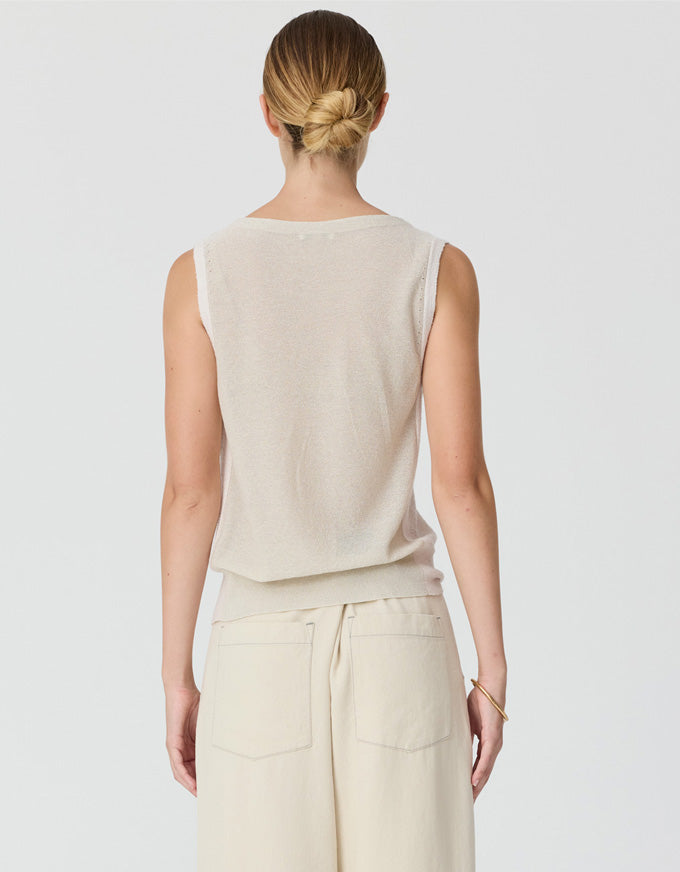 A woman shown from the back wearing a light beige sleeveless knit top and matching beige pants against a light gray studio background.