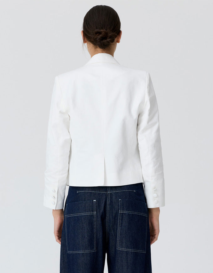 A model shown from the back wearing a white cropped blazer and dark blue jeans against a light gray studio background.