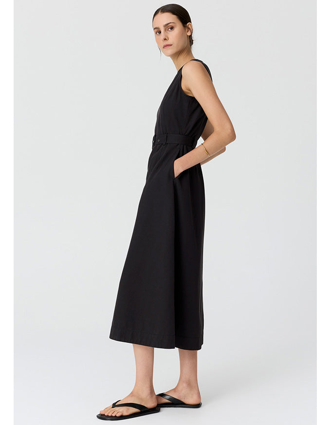 A woman modeling a sleeveless black midi dress with a matching waist tie, shown from a side profile against a light gray studio background.