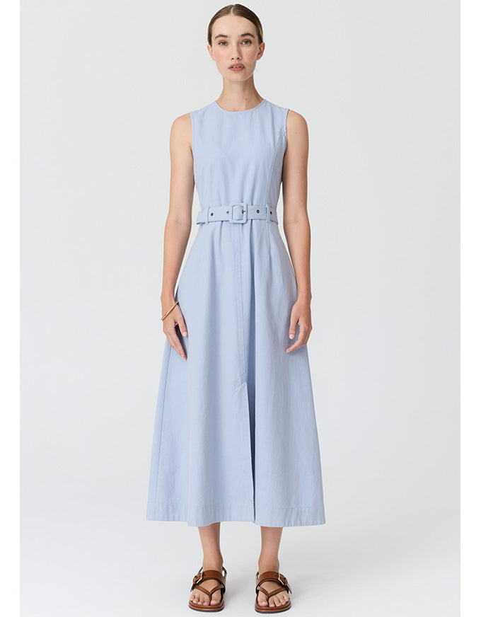 A woman modeling a sleeveless light blue midi dress with a matching belt, paired with brown sandals, against a plain light gray studio background.
