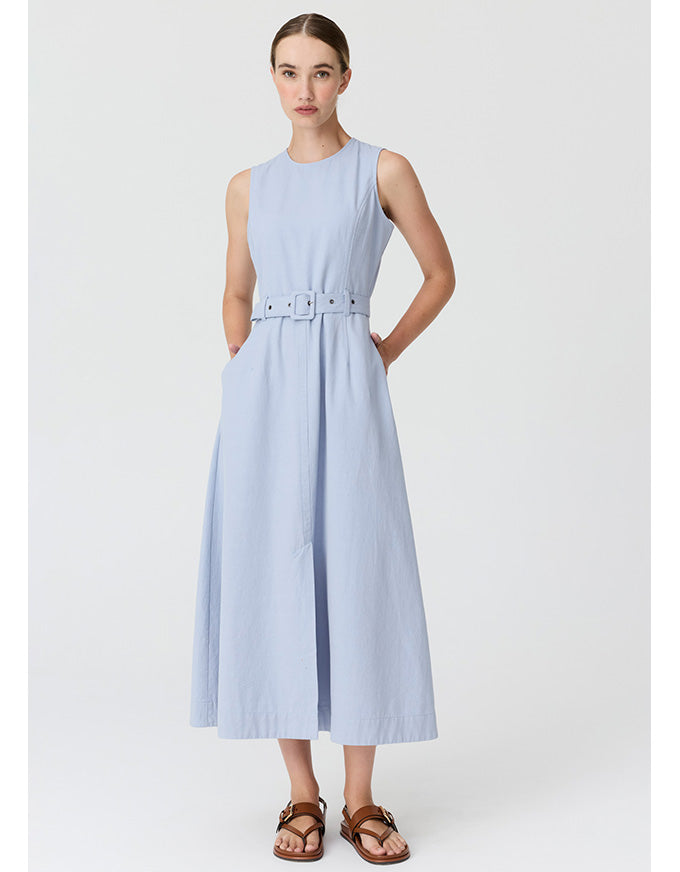 A woman modeling a sleeveless light blue midi dress with a matching belt and silver-tone buckle, paired with brown leather sandals, against a light gray studio background.