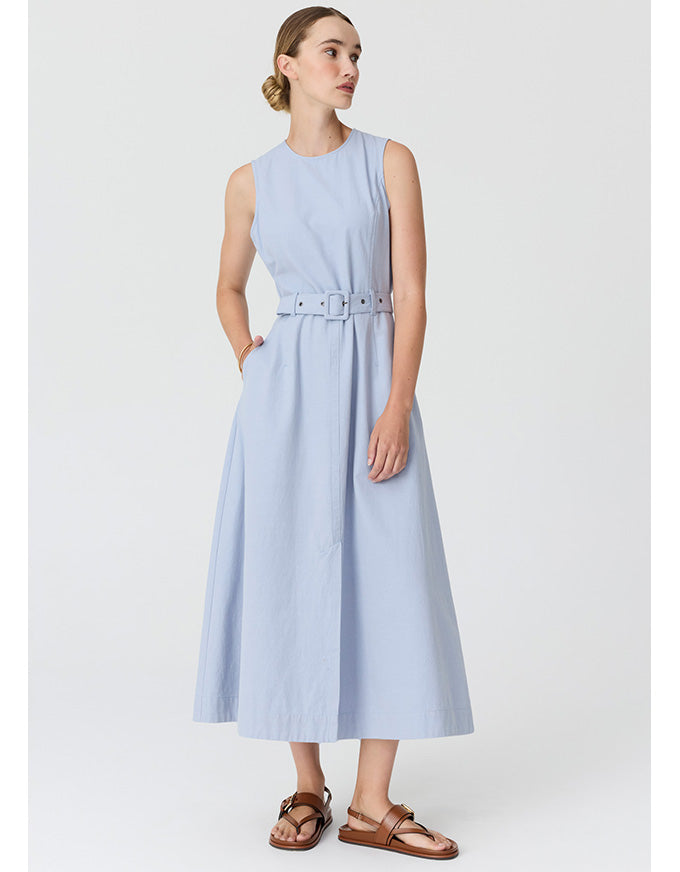 A woman modeling a sleeveless light blue midi dress with a matching belt, styled with brown leather sandals against a plain light gray studio background.