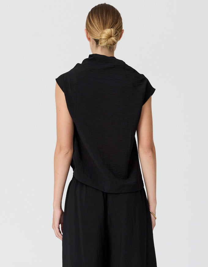 A woman shown from the back wearing a black sleeveless top and black wide-leg pants against a light gray studio background.