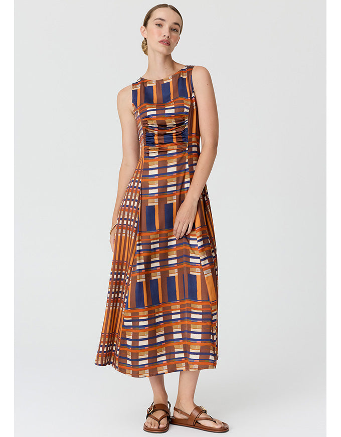 A woman modeling a sleeveless midi dress with a geometric plaid pattern in orange, navy blue, white, and brown, paired with brown leather sandals, against a light gray studio background.