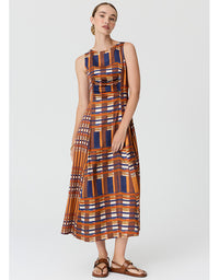 A woman modeling a sleeveless midi dress with a geometric plaid pattern in orange, navy blue, white, and brown, paired with brown leather sandals, against a light gray studio background.