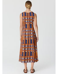 A woman viewed from the back wearing a sleeveless midi dress with a geometric plaid pattern in orange, navy blue, and white, paired with brown leather sandals, against a light gray studio background.