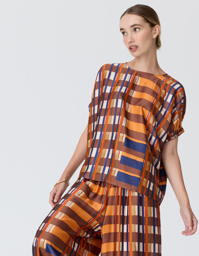 A woman modeling a matching two-piece set with a bold vertical stripe pattern in orange, brown, blue, and white, photographed against a solid light gray studio background.