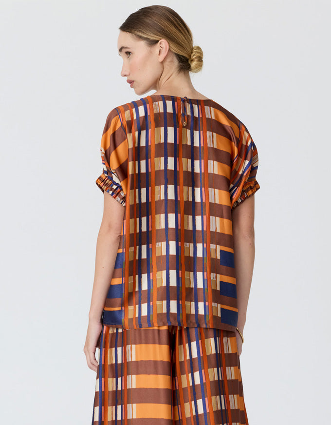 A woman shown from the back wearing a short-sleeve top and matching wide-leg pants with a bold vertical stripe pattern in orange, brown, navy, and cream, against a light gray studio background.