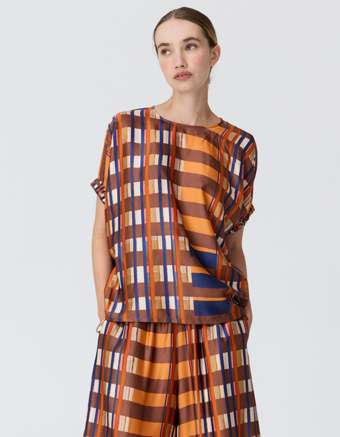 A model wearing a matching two-piece set with a bold orange, brown, and navy blue striped plaid pattern, photographed against a solid light gray background.
