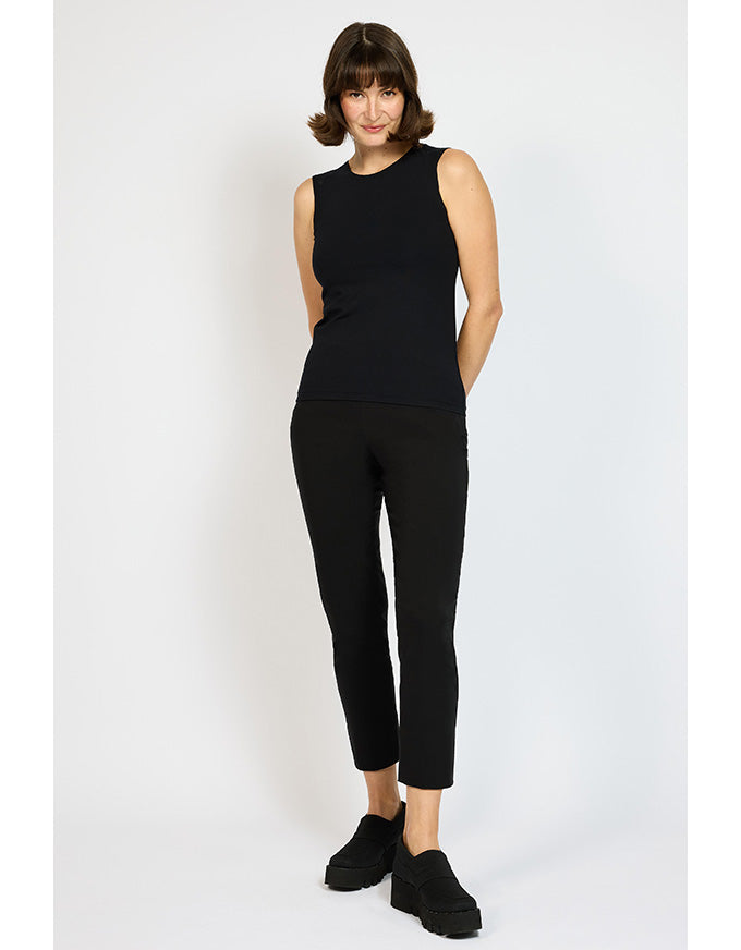 Woman wearing a black sleeveless top and black pants on a white background