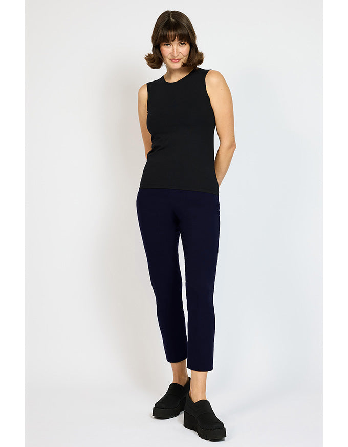Woman wearing a black sleeveless top and navy pants on a white background