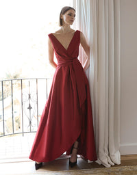Woman in a red evening gown standing in a room with large windows.