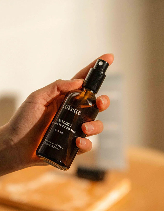 Hand holding a bottle of etikette Freycinet hair mask with a blurred background