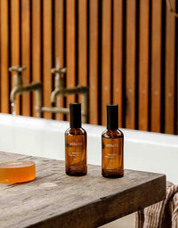 Two bottles of ethikens soap on a wooden surface with a bathtub and faucet in the background.