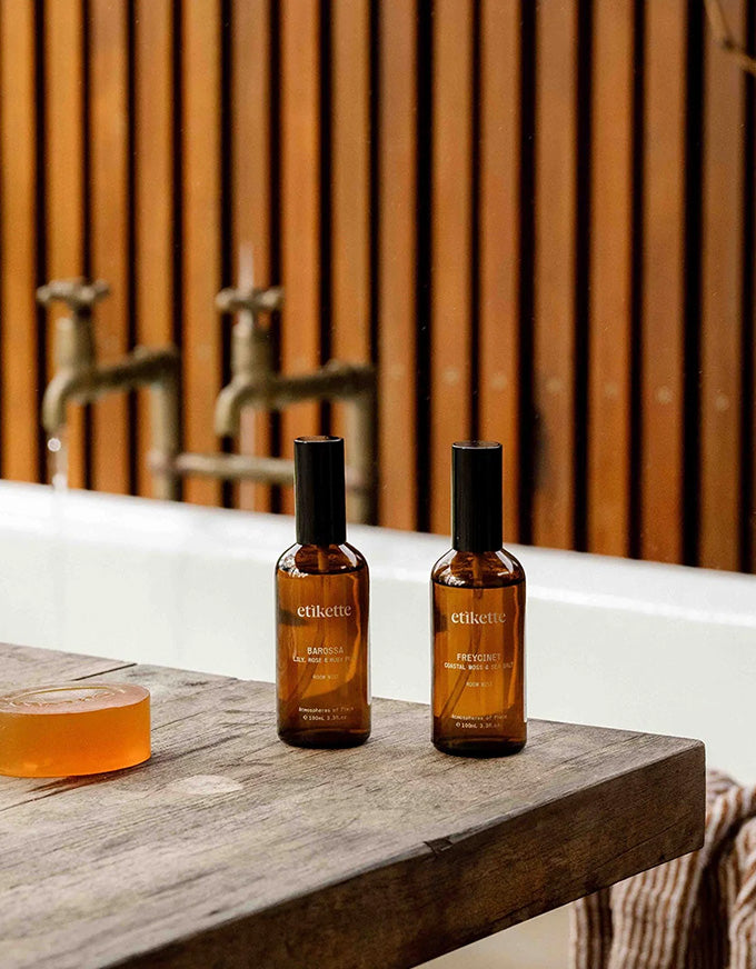 Two bottles of ethikens soap on a wooden surface with a bathtub and faucet in the background.