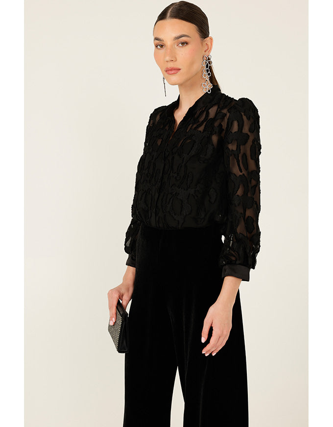 Woman wearing a black outfit with sheer sleeves against a beige background