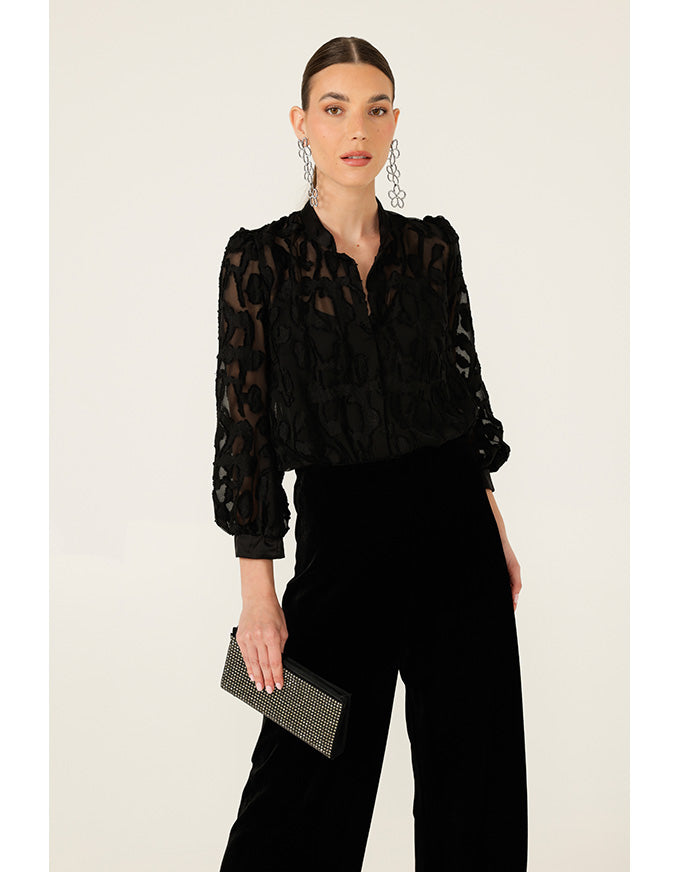 Woman wearing a black lace blouse and black pants with a neutral background