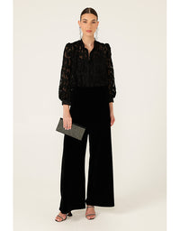 Woman wearing a black lace top and wide-leg pants holding a clutch on a white background