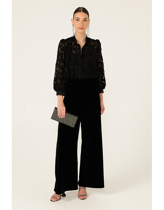 Woman wearing a black lace top and wide-leg pants holding a clutch on a white background