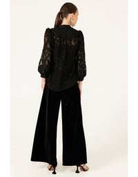 Woman wearing a black lace blouse and black pants on a white background