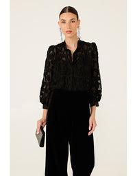 Woman wearing a black lace blouse and black pants on a beige background