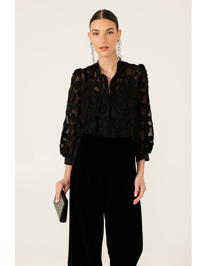 Woman wearing a black lace blouse and black pants on a beige background