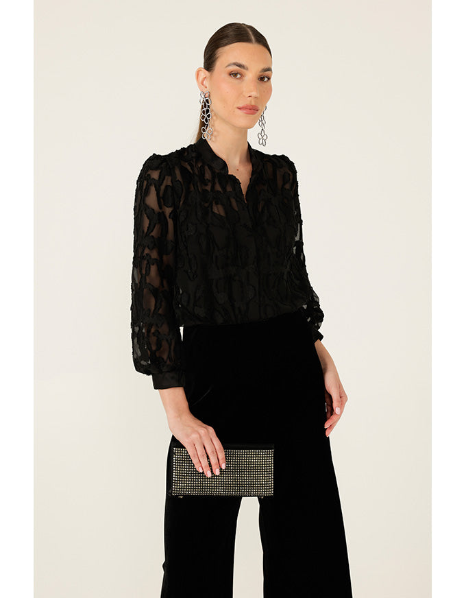 Woman wearing a black lace blouse and black pants with a clutch against a white background