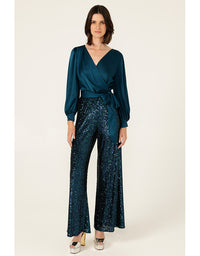 Woman wearing a teal wrap top and sequin pants on a white background