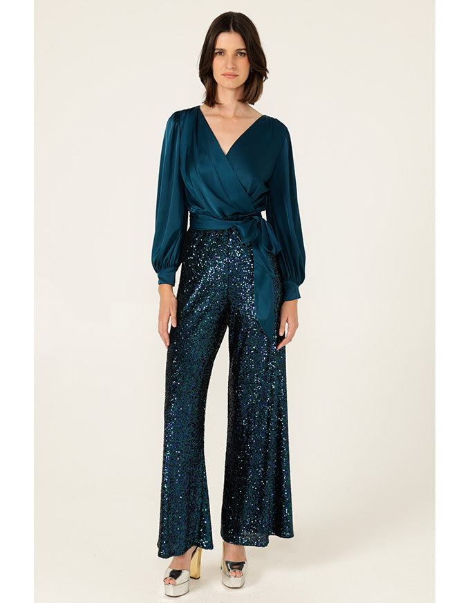 Woman wearing a teal wrap top and sequin pants on a white background