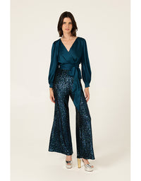 Woman wearing a teal top and sequin pants on a white background