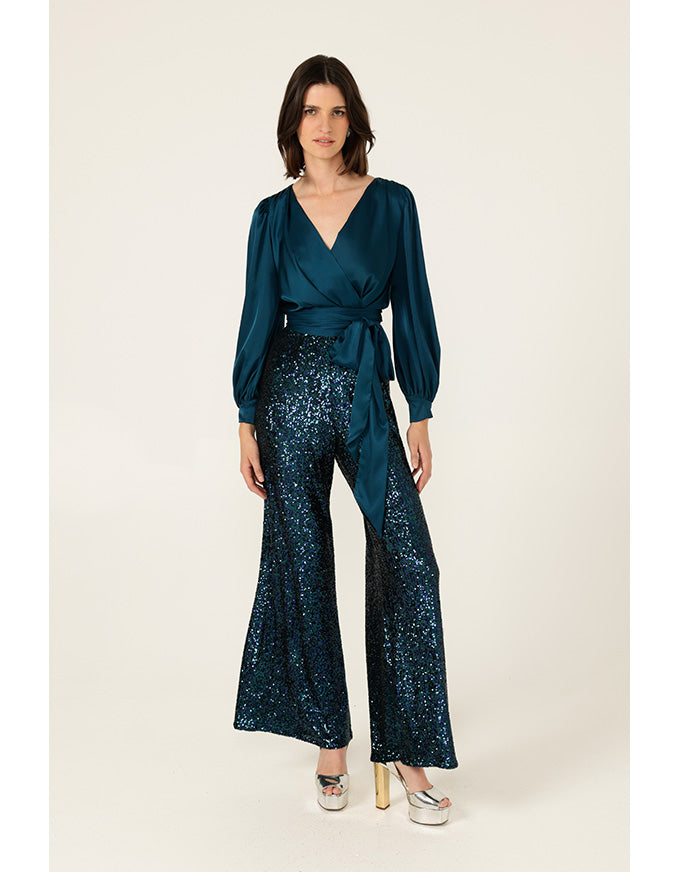 Woman wearing a teal top and sequin pants on a white background