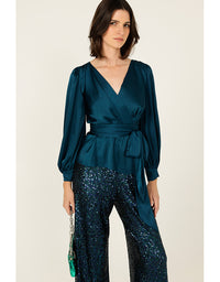 Woman wearing a teal top and sequin pants on a beige background