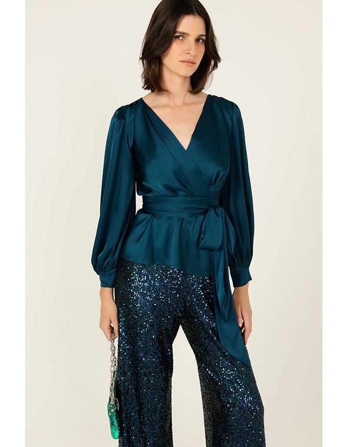 Woman wearing a teal top and sequin pants on a beige background