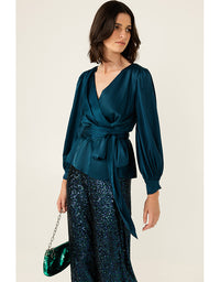 Woman wearing a teal satin top and sequin pants with a neutral background